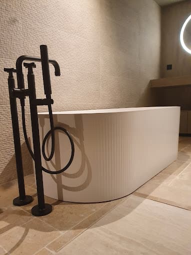 Baignoire îlot et robinetterie sur pied noire posées dans une salle de bain en pierre