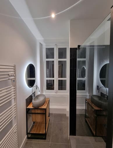 Salle de bain avec double vasque à poser sur meuble bois et miroirs ronds rétroéclairés